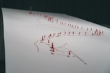 A large sheet of paper is marked with interconnected lines, each intersection punctuated by a red pushpin. The pushpins are densely placed, indicating specific locations, and the lines suggest routes or connections between these points.