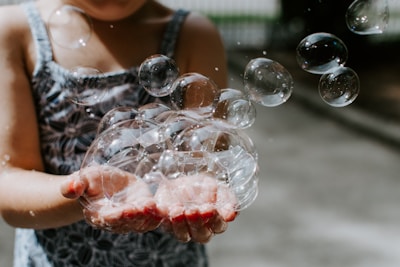 Close-up of a child’s hands holding a bright yellow bubble wand with bubbles floating around.