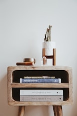 books in brown wooden side table beside white wall