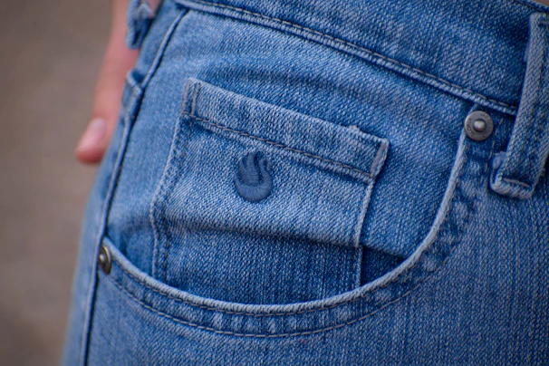 Dark denim jeans with rugged stitching and a small jymi blatz emblem on the pocket.