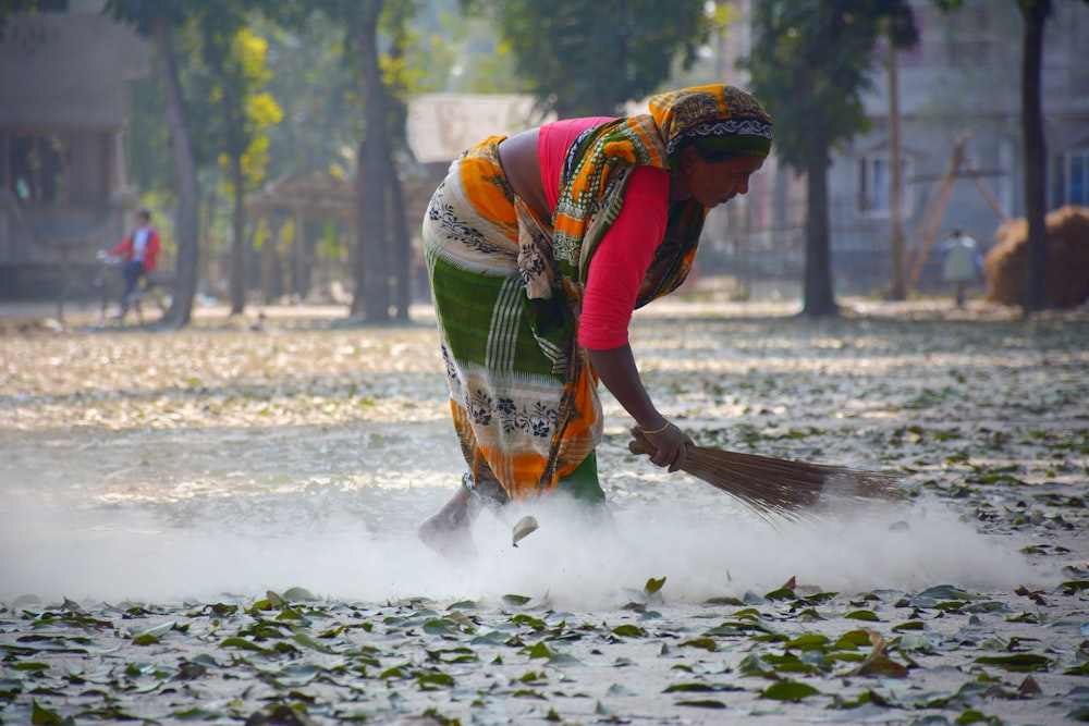 woman in multicolored dress sweeping leaves