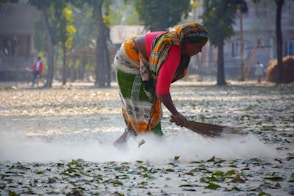 woman in multicolored dress sweeping leaves