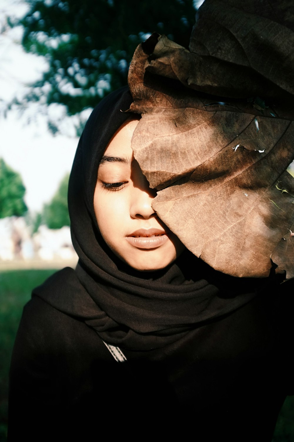 woman in black traditional dress behind dried brown leaf