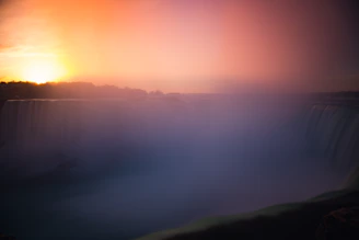 A dramatic sunset over a misty waterfall surrounded by lush rainforest.