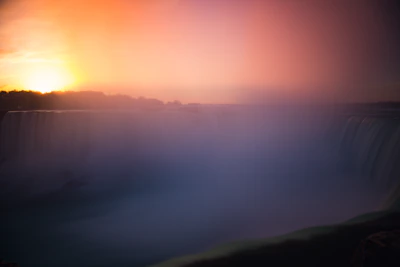 A vibrant sunset over a misty waterfall deep in a Latin American rainforest.