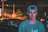 A young man wearing an oversized dark t-shirt with a sleek urban background at dusk.