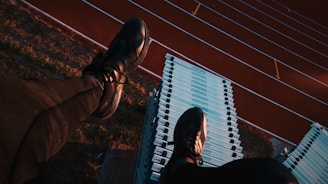 A person wearing black athletic shoes and pants is sitting on top of a stack of white sports hurdles. Below, a running track with red lanes is visible, creating a contrast with the blue and white hurdles.
