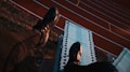 A person wearing black athletic shoes and pants is sitting on top of a stack of white sports hurdles. Below, a running track with red lanes is visible, creating a contrast with the blue and white hurdles.