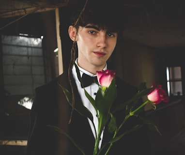 man wearing black and white formal suit holding two red roses