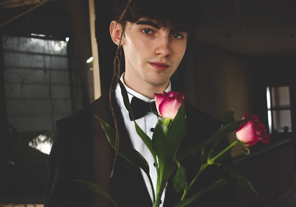 man wearing black and white formal suit holding two red roses