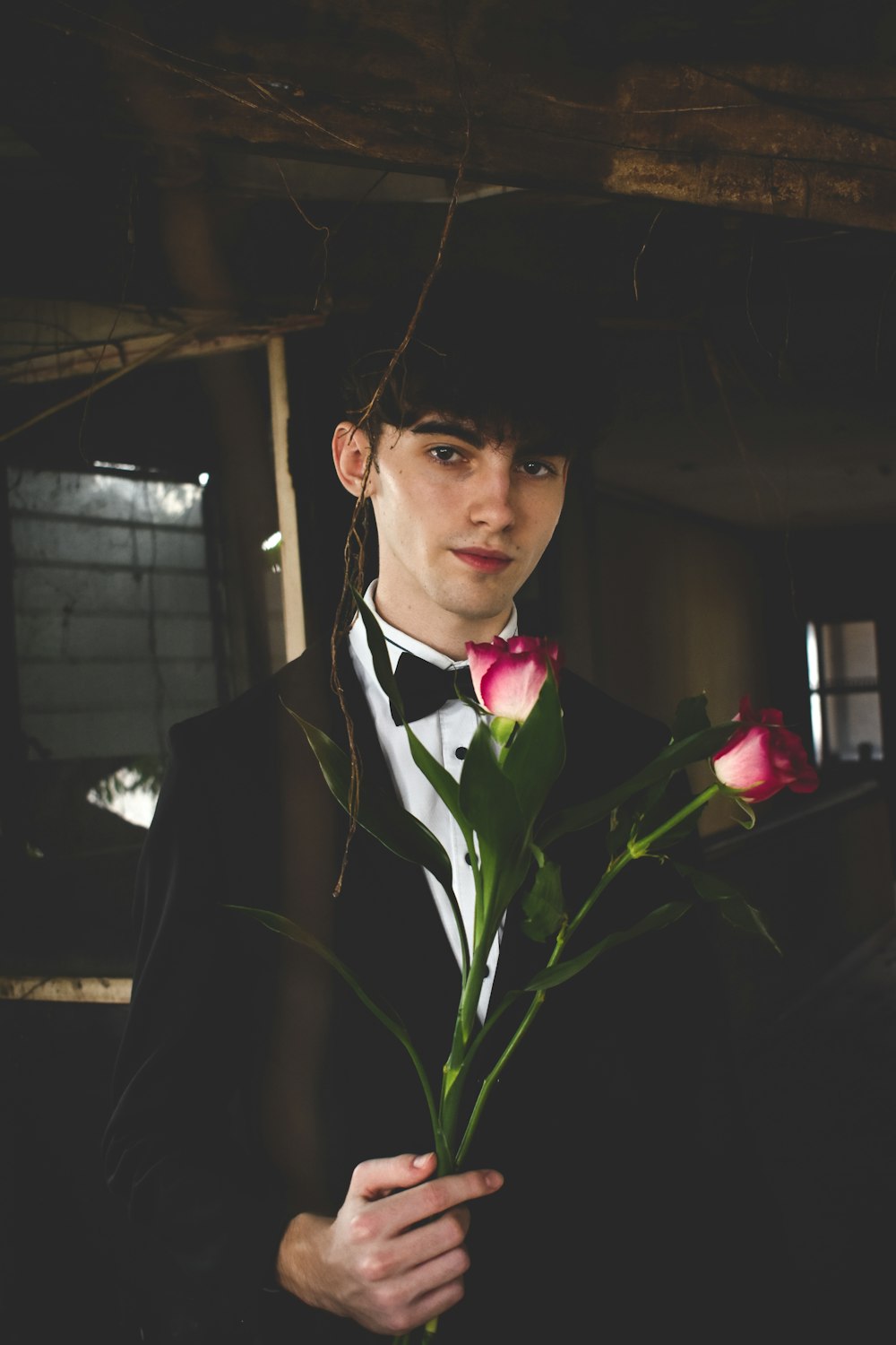 man wearing black and white formal suit holding two red roses