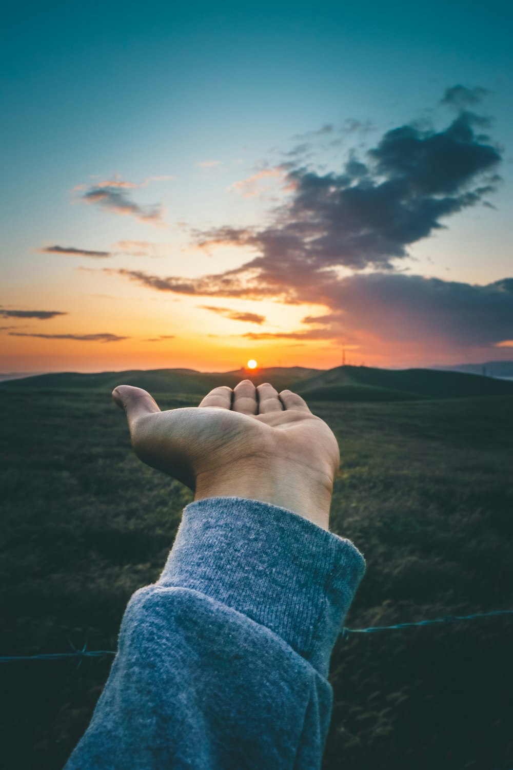 force-perspective photography of person wearing gray long-sleeved shirt carrying sun setting behinds haze