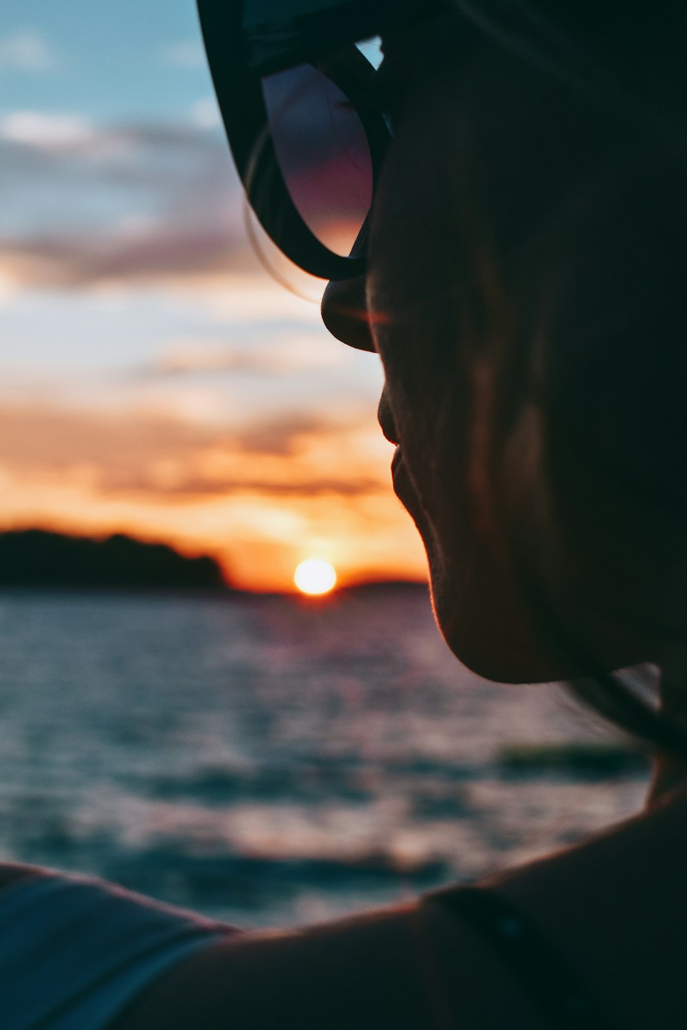donna in occhiali da vista con montatura nera vicino allo specchio d'acqua durante il tramonto