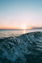 A serene ocean horizon at sunset with gentle waves reflecting warm colors.