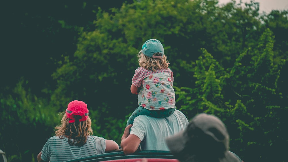 girl riding man's shoulder beside girl near trees during day