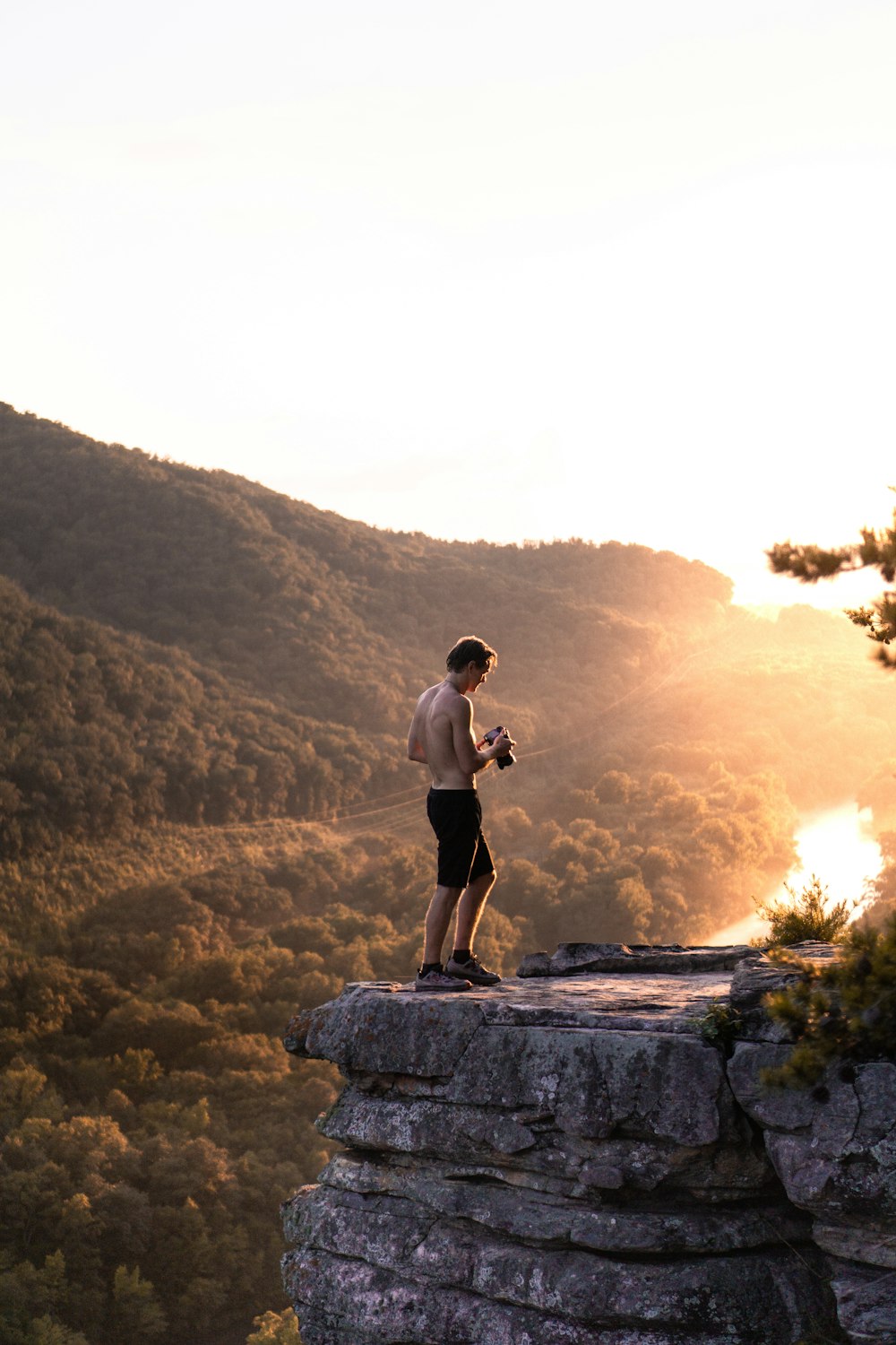 topless man in black shorts standing near cliff at daytime
