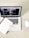 A laptop displaying a webpage with various tabs open. In front of the laptop, there is a closed notebook with a speckled cover and a pink pen resting on it. A white wireless mouse is positioned on the right side of the laptop, all set on a light wooden surface.