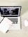 A laptop displaying a webpage with various tabs open. In front of the laptop, there is a closed notebook with a speckled cover and a pink pen resting on it. A white wireless mouse is positioned on the right side of the laptop, all set on a light wooden surface.
