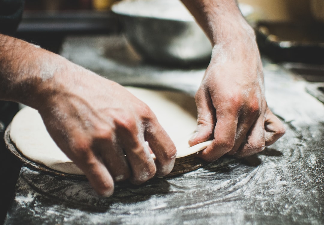 a person is kneading dough on a table, pizza preparation