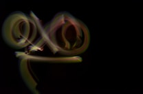 The photograph features light trails that create abstract patterns against a completely dark background. The trails appear to form looping and swirling shapes, with varying intensities and colors blending into each other.