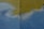 A textured wall with a combination of faint blue and yellow paint. There is a vertical crack running through the middle of the wall. The paint appears to have been applied unevenly, with some areas blending together.