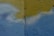A textured wall with a combination of faint blue and yellow paint. There is a vertical crack running through the middle of the wall. The paint appears to have been applied unevenly, with some areas blending together.