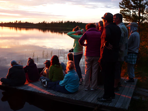 A serene view of Müritz lakes with workshop attendees discussing ideas on a wooden dock at sunset.