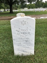 A white marble tombstone in a cemetery displays the Star of David and commemorates a World War II veteran named Myron E. Berrick, indicating his rank as First Lieutenant in the US Army. Surrounded by green grass and rows of similar tombstones, the setting is serene and solemn.