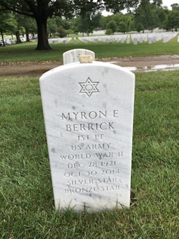 A white marble tombstone in a cemetery displays the Star of David and commemorates a World War II veteran named Myron E. Berrick, indicating his rank as First Lieutenant in the US Army. Surrounded by green grass and rows of similar tombstones, the setting is serene and solemn.