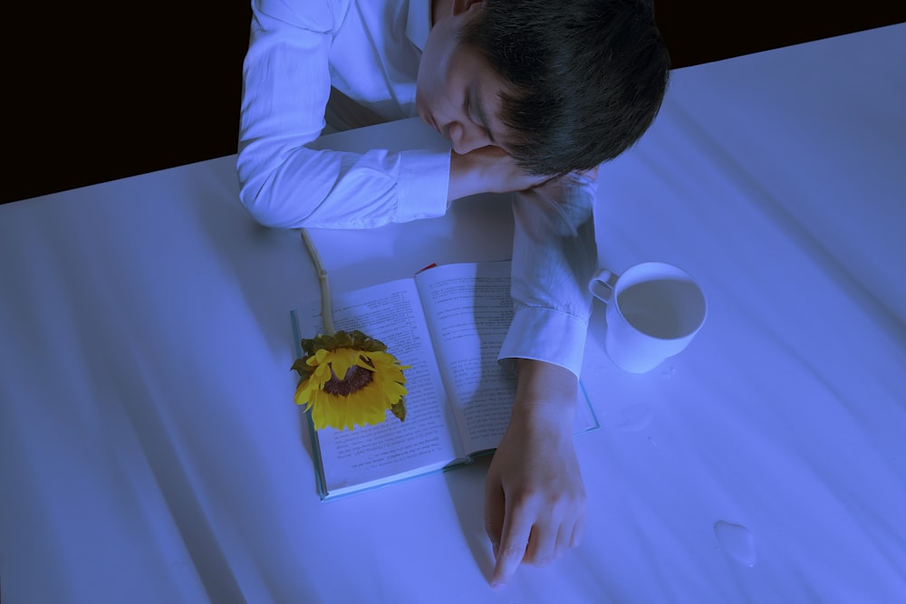 uomo in camicia bianca appoggiato al tavolo accanto al libro e alla tazza