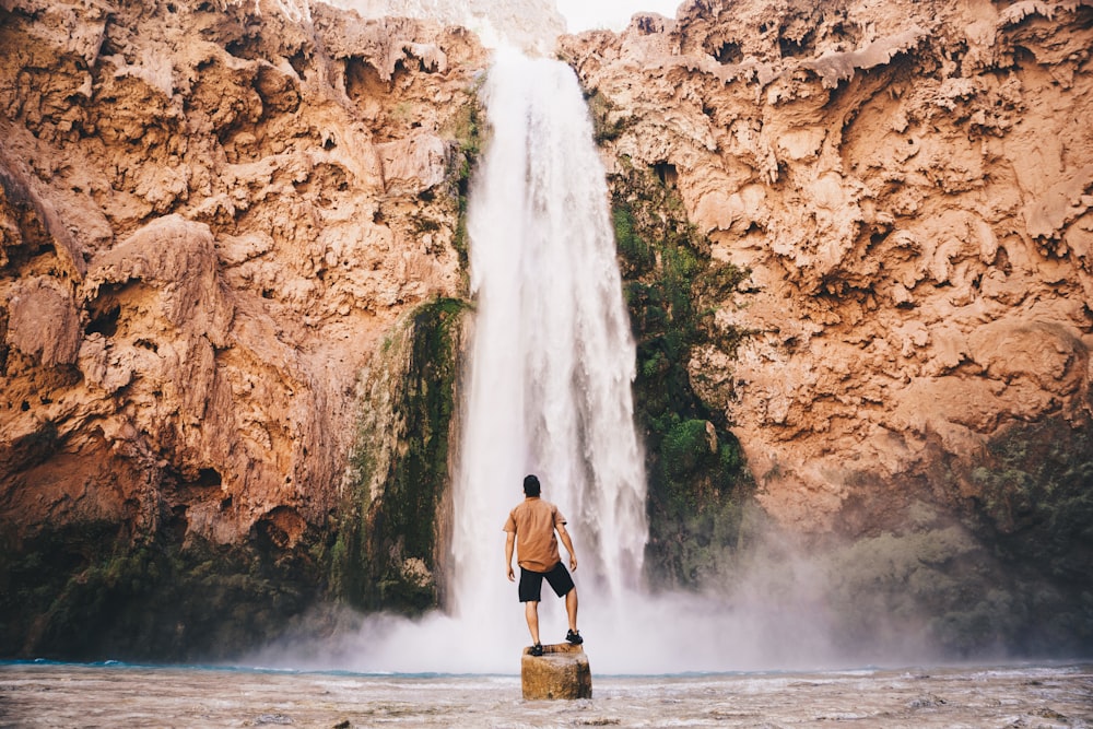 Hombre de pie sobre piedra frente a la cascada