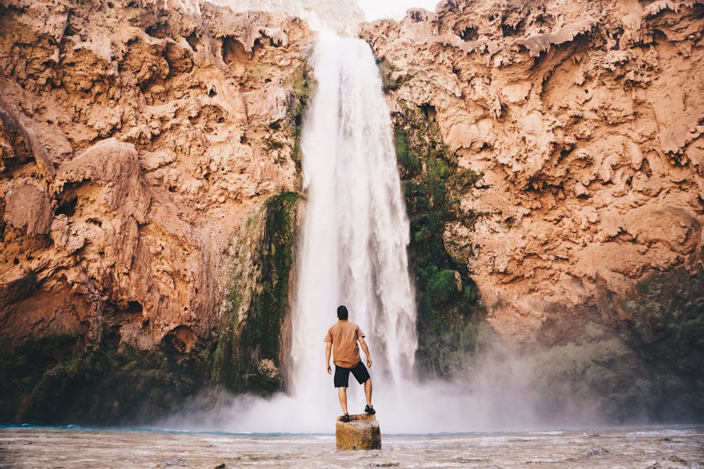 Mann steht auf Stein vor Wasserfall