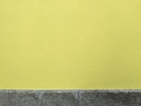 A textured yellow wall above a rough, gray stone base. The surface has a subtle stucco pattern, and the stones have a slightly weathered appearance.