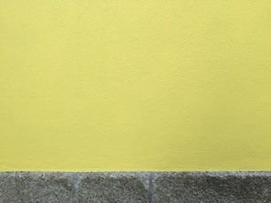 A textured yellow wall above a rough, gray stone base. The surface has a subtle stucco pattern, and the stones have a slightly weathered appearance.