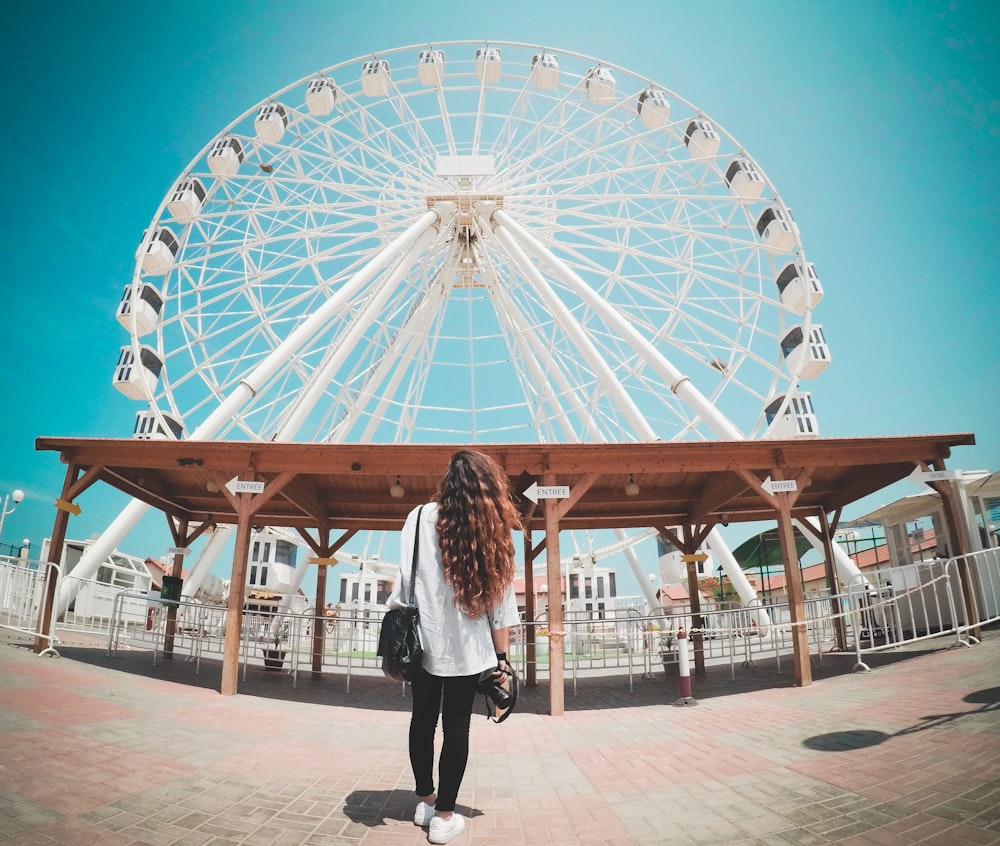 Mulher de cabelos compridos olha para a roda-gigante branca dentro do parque de diversões