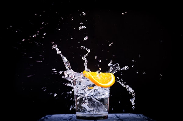 Water splashing upwards from a glass with a slice of orange on the rim.
