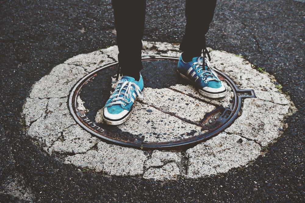 person wearing blue-and-white sneakers standing on pavement at daytimew