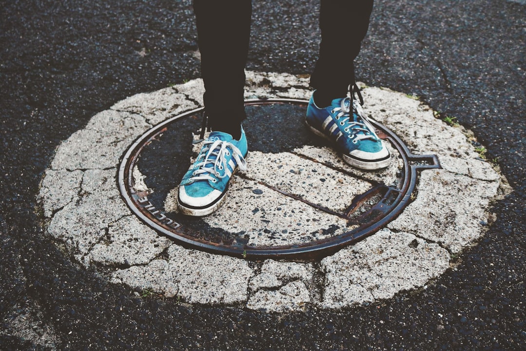 person wearing blue-and-white sneakers standing on pavement at daytimew