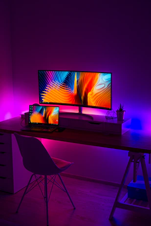 A sleek laptop and desktop setup with colorful peripherals on a modern desk in a bright room.