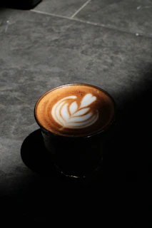 A steaming latte with heart-shaped latte art served alongside a small glass of water
