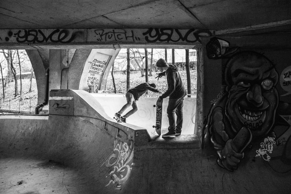 grayscale of two people on skateboard bowl