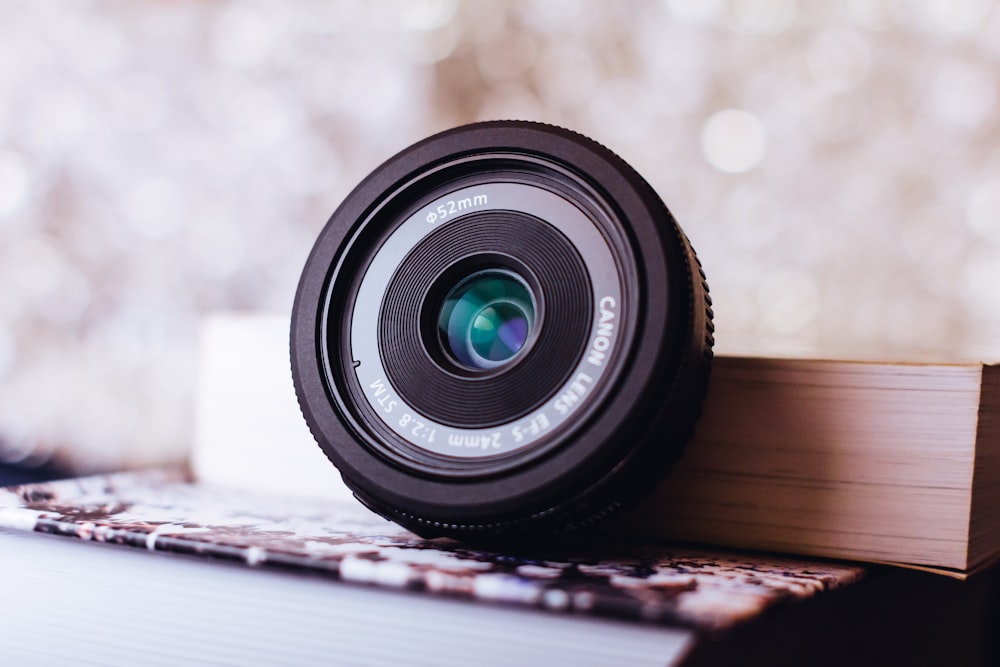 black Canon camera lens leaning on white book