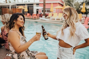 woman on pool tosing liquor with woman at daytime