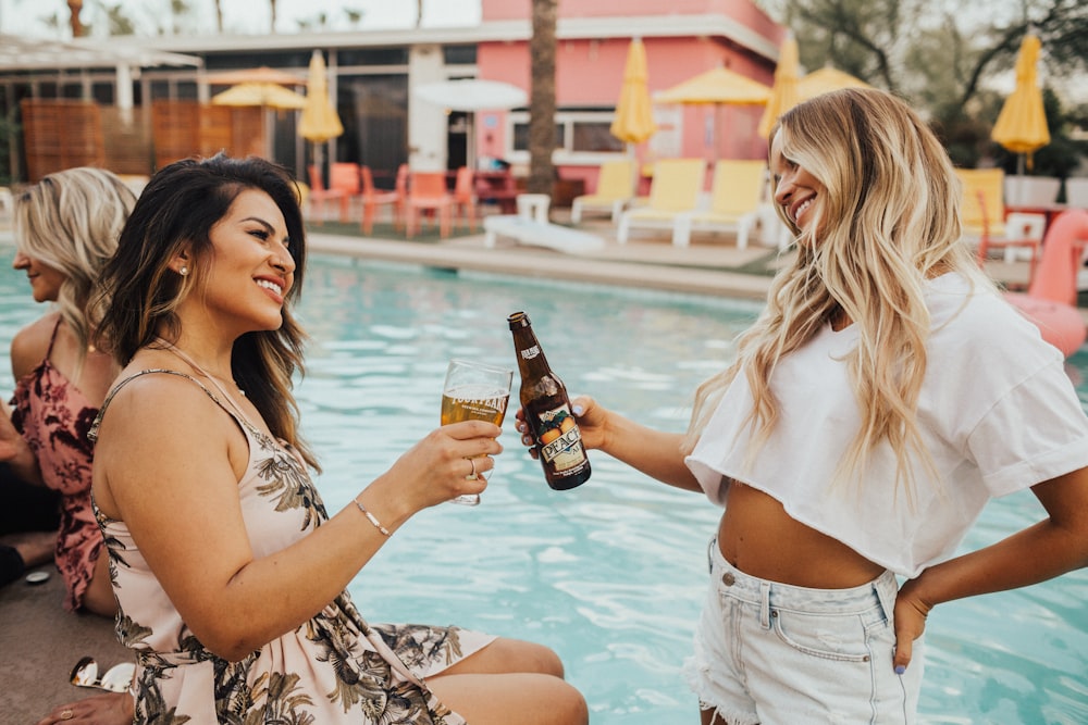 woman on pool tosing liquor with woman at daytime