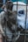 A close-up of a dog with light fur and a striking blue eye, partially obscured by the bars of a cage. The dog appears calm yet slightly somber, with its head partially turned, giving focus to its expressive eye.