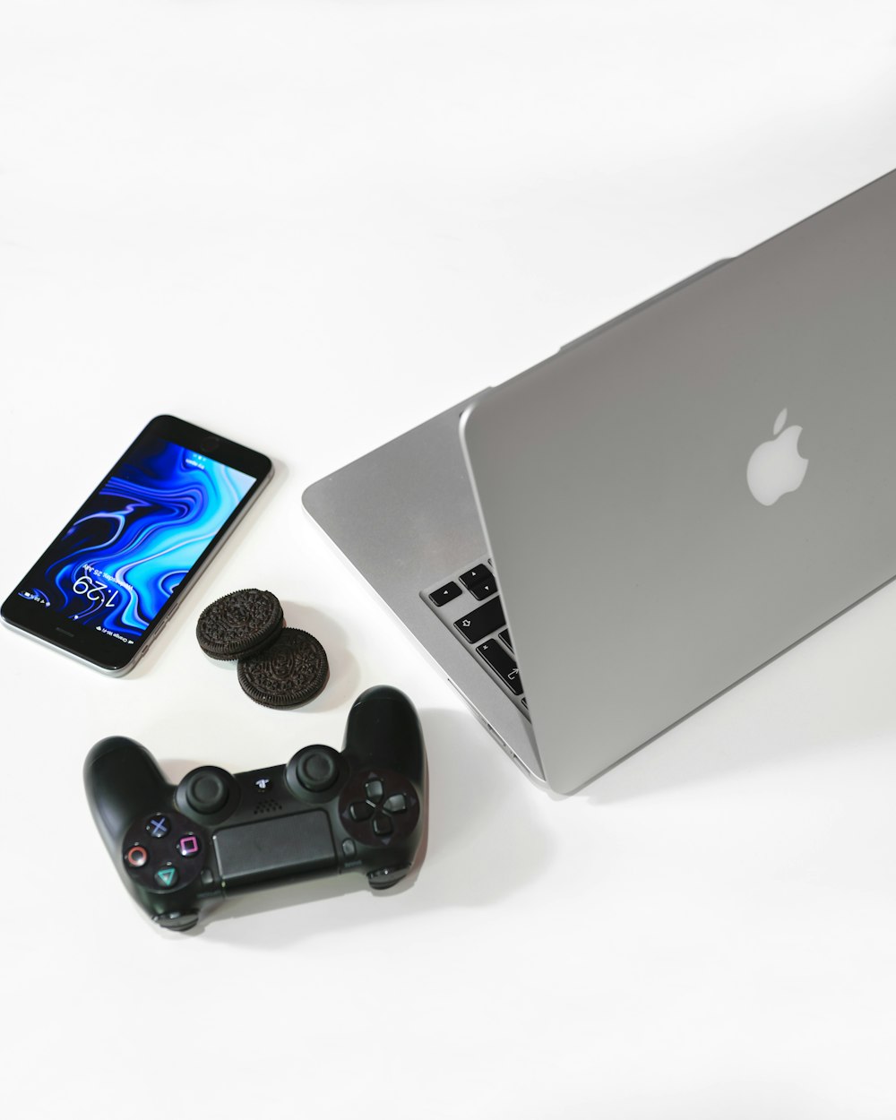 silbernes MacBook neben schwarzem Sony-Gamepad
