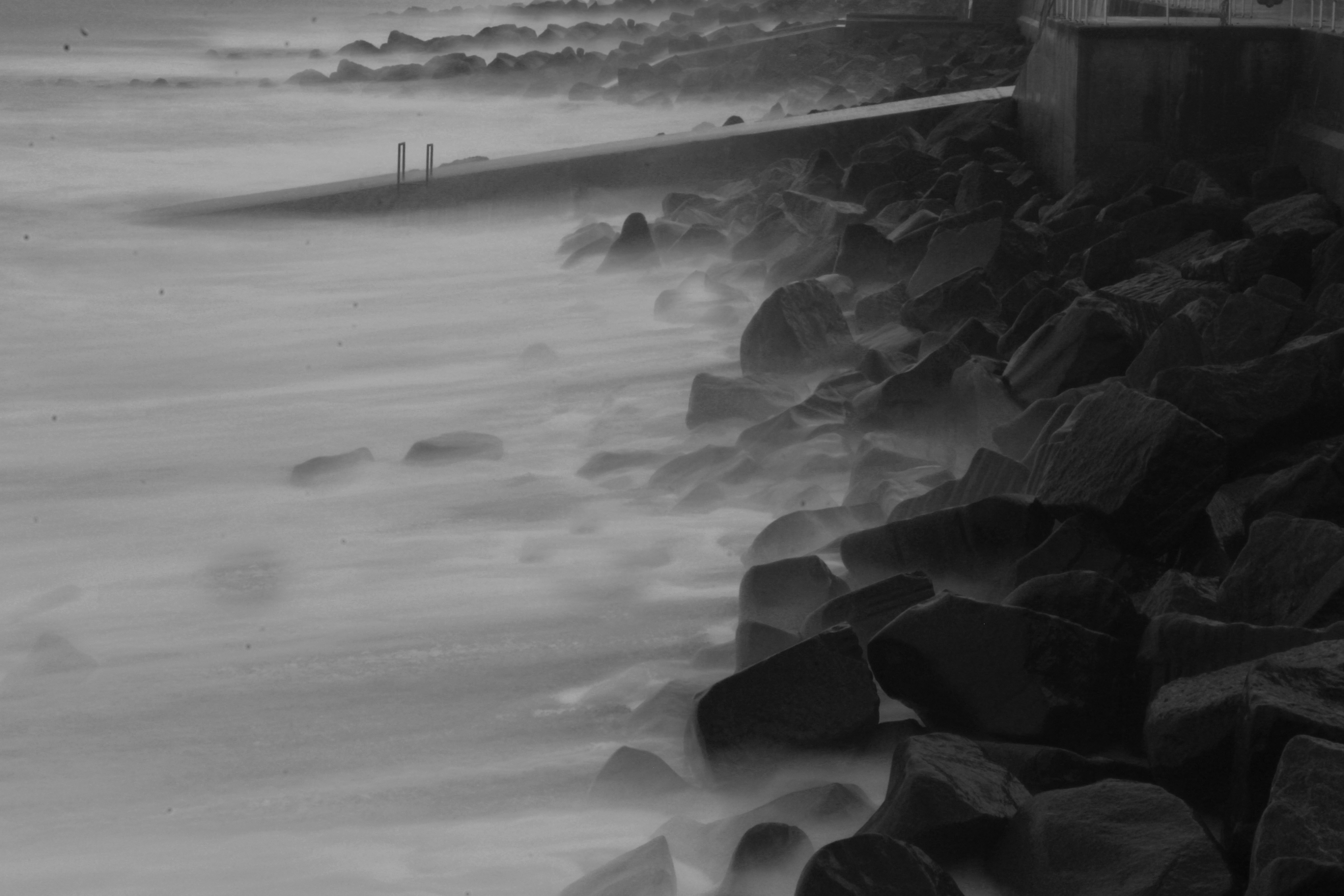 grayscale photo of waves rushed at bay long exposure zoom background