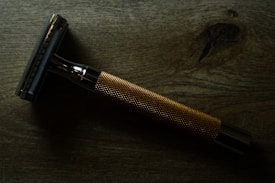 A metal safety razor is placed on a wooden surface. The razor has a shiny, metallic finish with a textured grip handle.