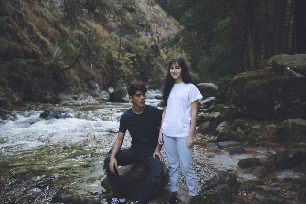 man in blue shirt sitting beside woman in white shirt standing on river