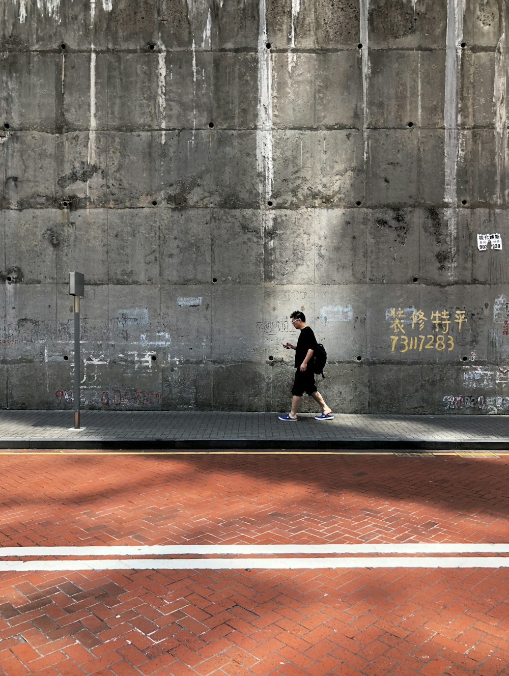 hombre caminando al lado de la pared y la calle durante el día